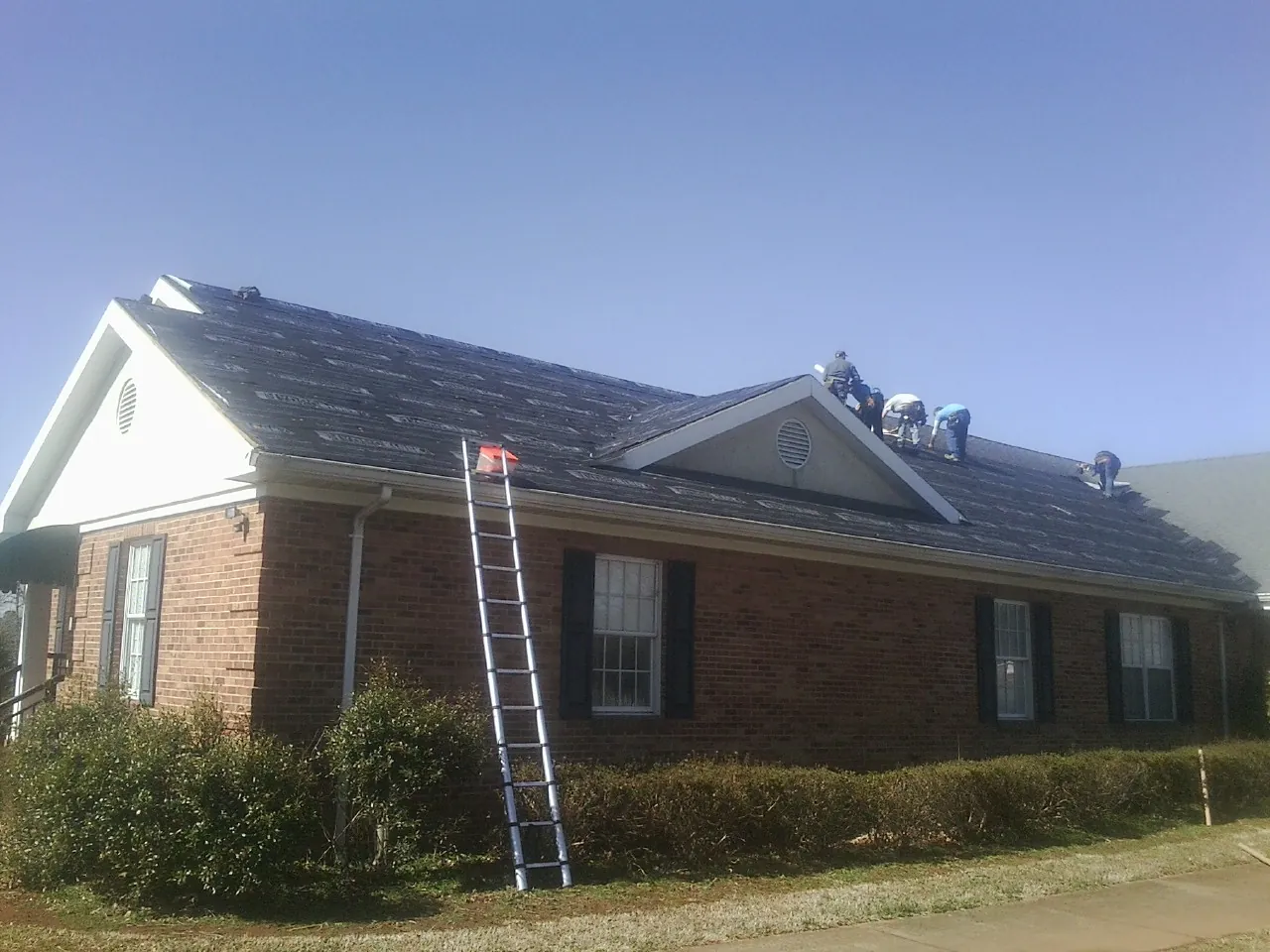 Crew tearing shingles off a brick ranch roof with a ladder set — Emergency Roof Repair work by our crew in Granby