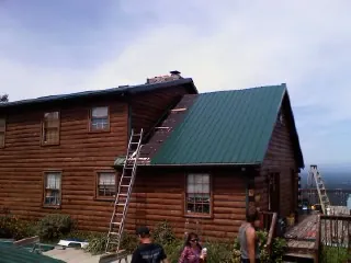 Green metal roof going on a two story log home with ladders set in Granby