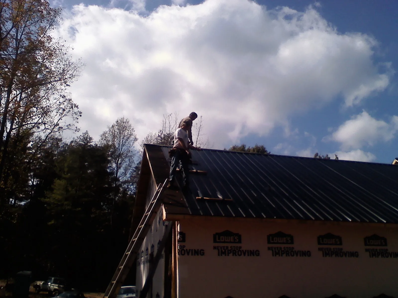 Roofer fastening dark metal panels high against a cloudy sky, from a Roof Inspection job in Granby